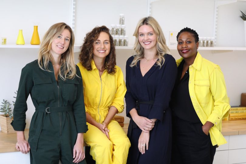 4 women sitting or leaning on a counter, smiling for the camera.