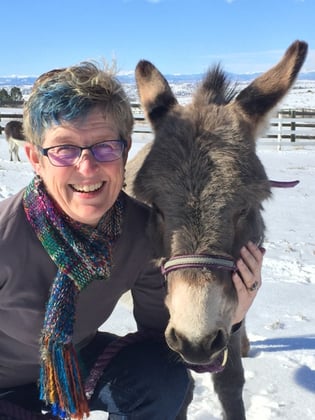 Lisa Crispin kneeling next to a donkey. She has her hand on the side of it's face.