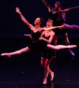 4 ballerinas in black, dancing on a stage.