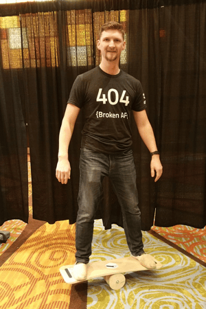 A man wearing a black t shirt that says 404 {broke AF} and he's standing on a balance board.