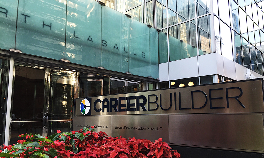 The outside front of a large office building with poinsettias in front of a metal sign that says Career Builder.