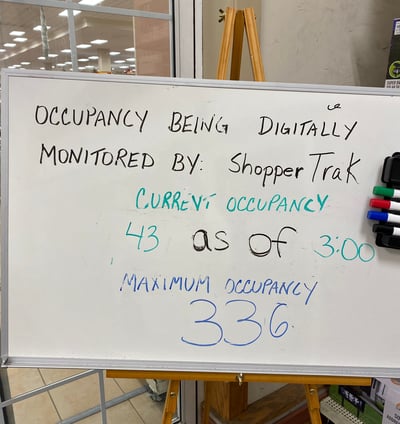 A white board on an easel which says occupancy being digitally monitored by: Shopper Trak current occupancy 43 as of 3:00.