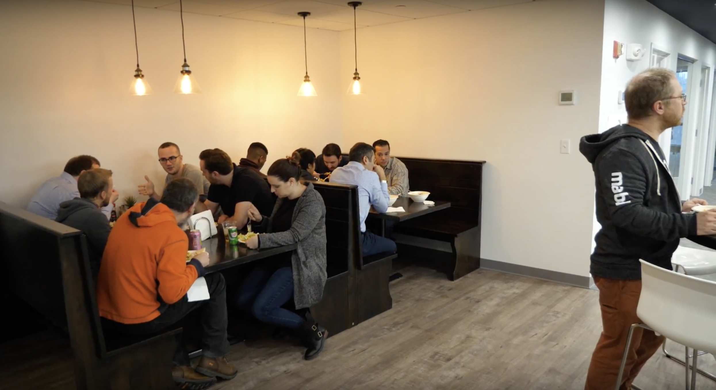 Several people sitting at booths in a restaurant eating and one man standing at a bar.