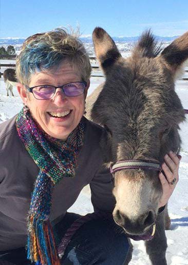 Lisa Crispin kneeling next to a donkey. She has her hand on the side of it's face.